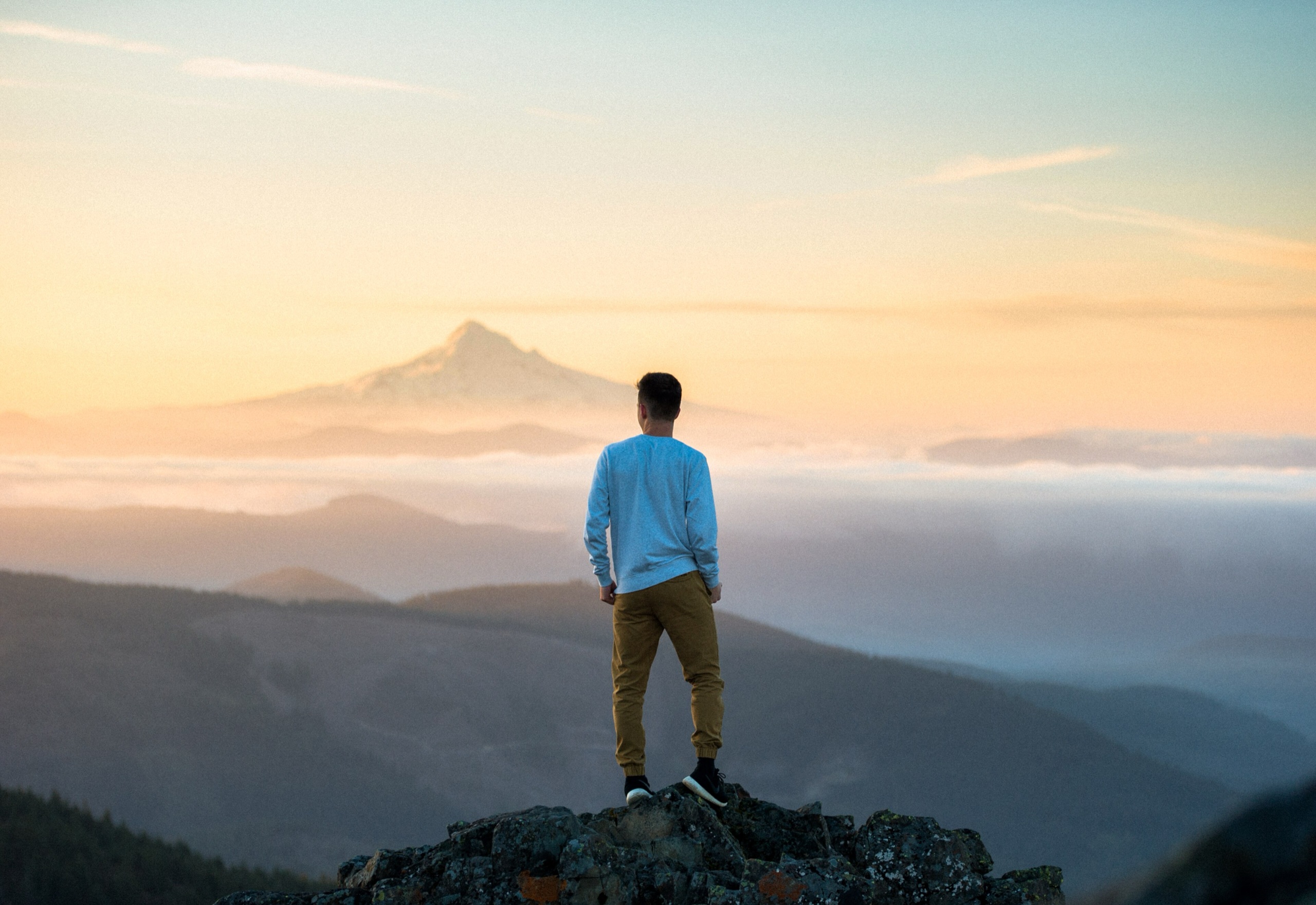 A hiker standing on a mountain summit at sunrise, above the clouds